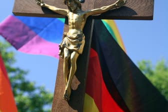 Eine Regenbogenfahne und Jesuskreuz (Symbolbild): Auf der umstrittenen Petitionsplattform Citizengo soll die Teilnahme der katholischen Kirche am CSD verhindert werden.