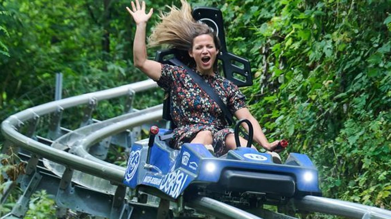 Eine Frau fährt auf der Sommer-Rodelbahn in Marzahn-Hellersdorf. Sie hebt ihre Hand, ihre Haare fliegen durch den Wind.