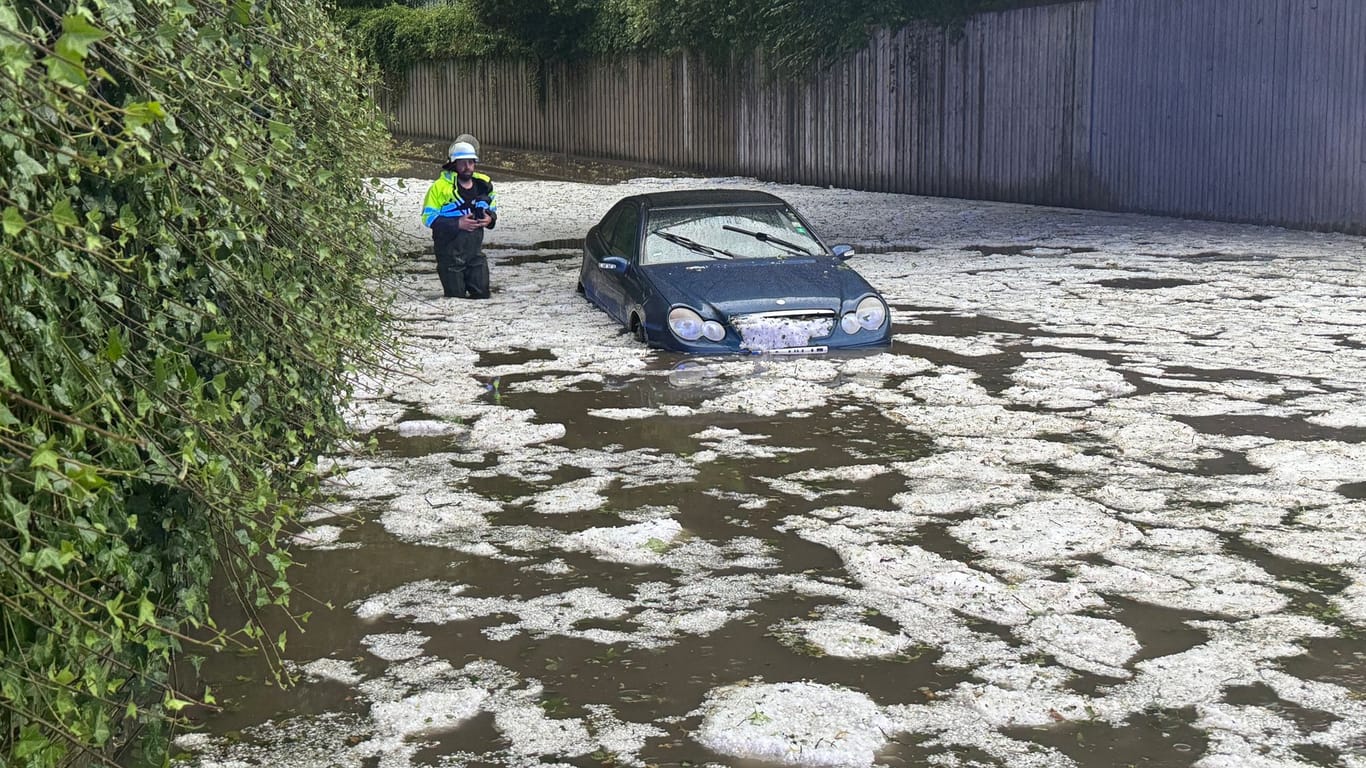 Nach schweren Unwettern steht ein Auto in Bayern auf einer überfluteten Straße, in der Hagelkörner treiben. Auch in Niedersachsen kam es zu Überschwemmungen.