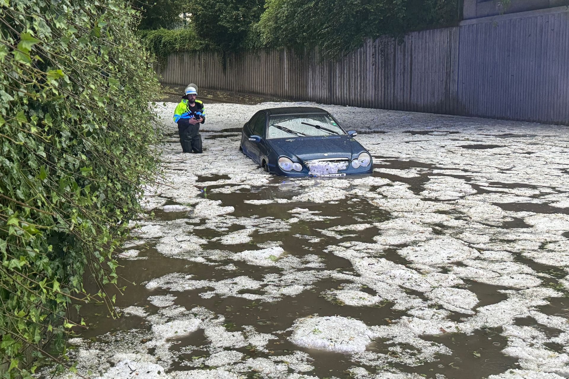 Nach schweren Unwettern steht ein Auto in Bayern auf einer überfluteten Straße, in der Hagelkörner treiben. Auch in Niedersachsen kam es zu Überschwemmungen.