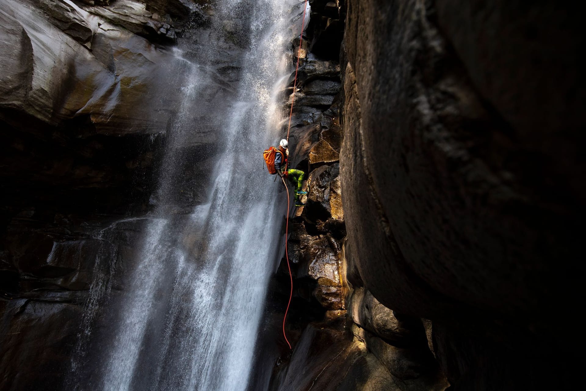 Ein Canyoning-Sportler klettert einen Wasserfall hoch.