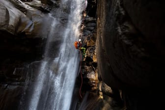 Ein Canyoning-Sportler klettert einen Wasserfall hoch.