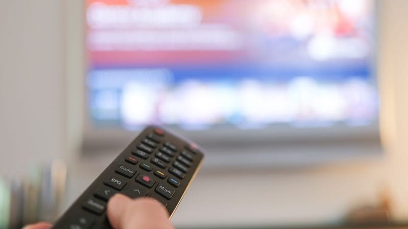 Eine Hand bedient eine Fernbedienung für ein TV-Gerät: Verträge über TV-Kosten haben zu Abmahnungen geführt.