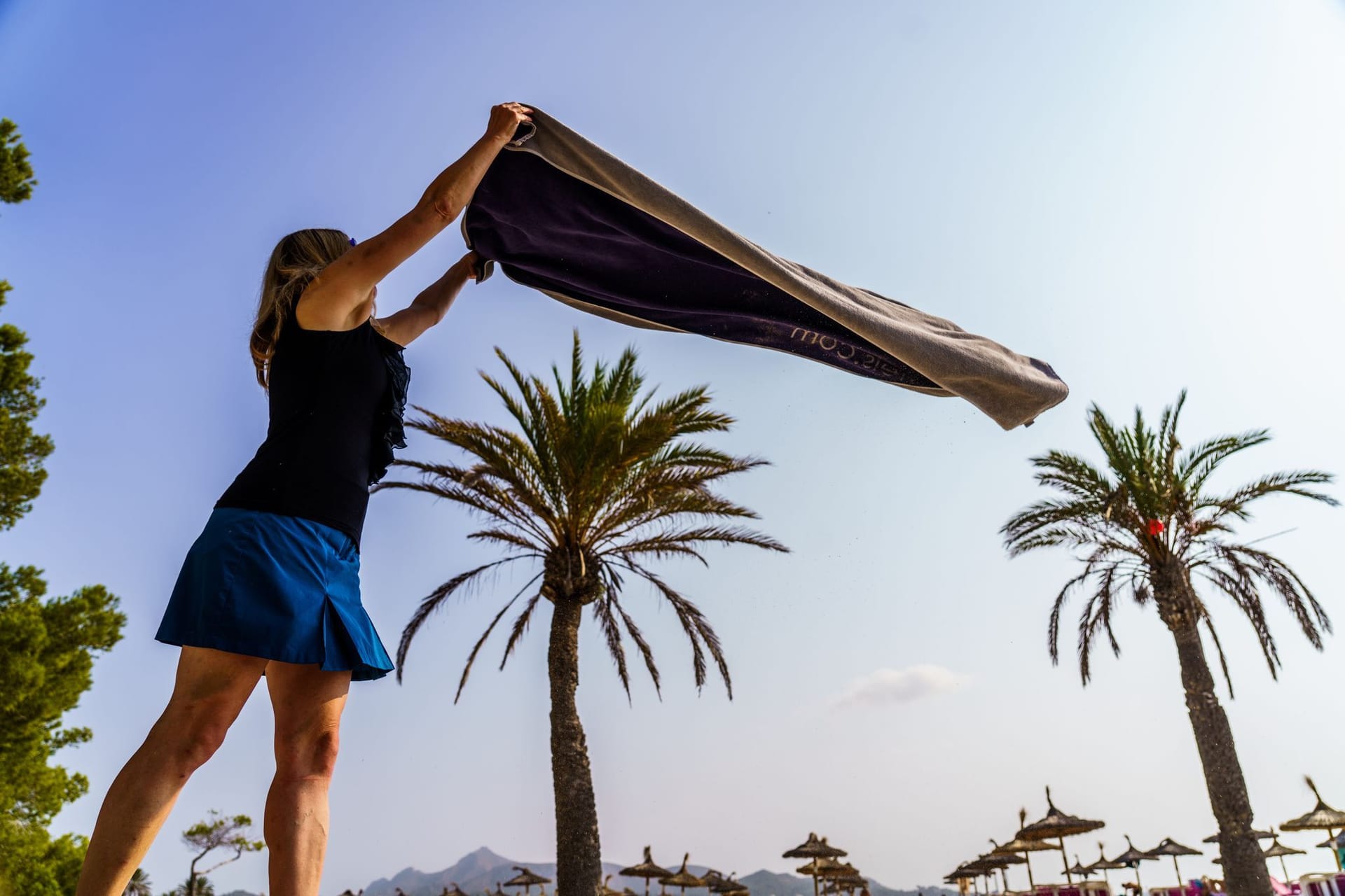 Eine Frau breitet am Strand ihr Handtuch aus Eine Frau breitet am Strand ihr Handtuch aus