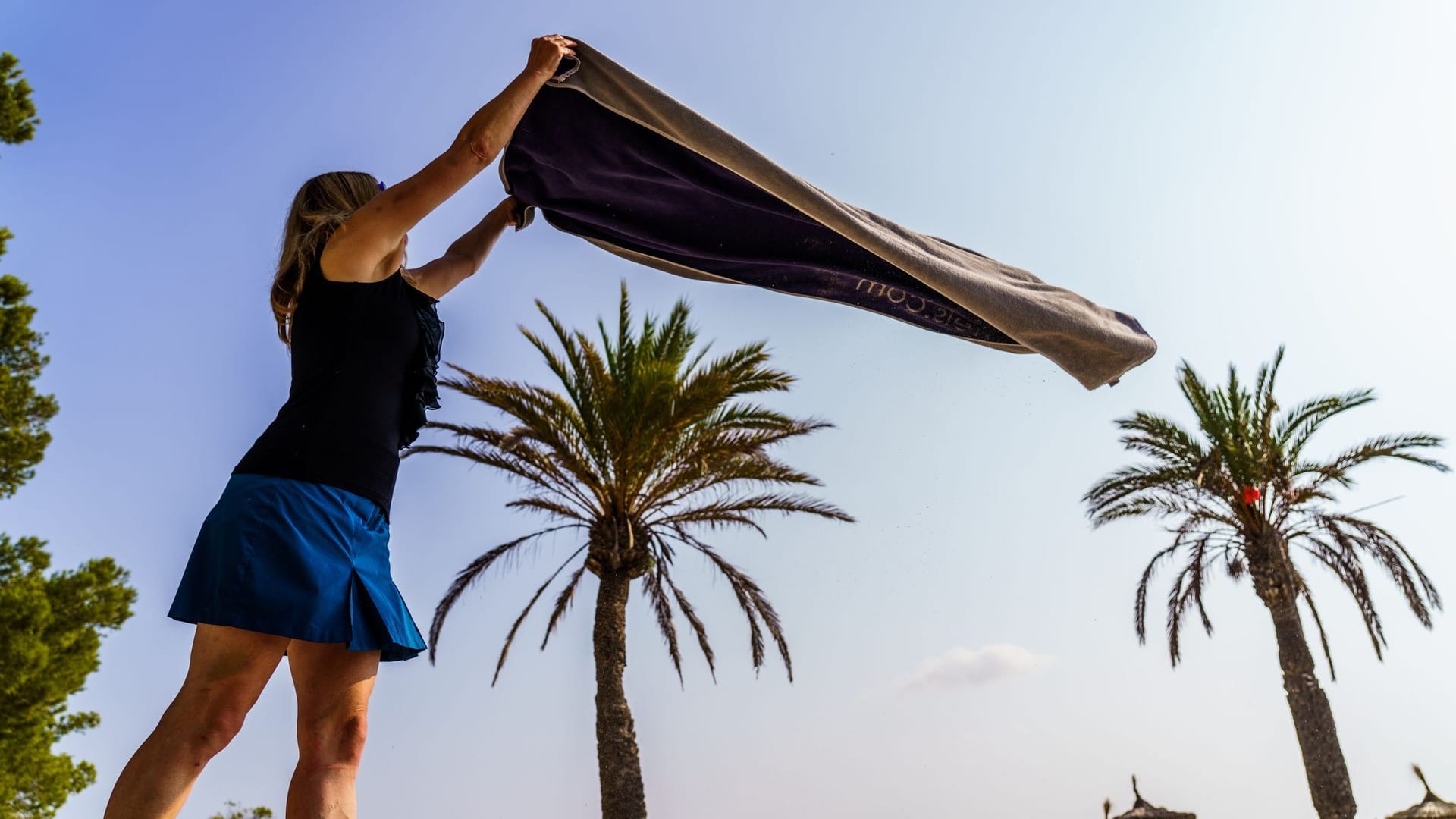 Eine Frau breitet am Strand ihr Handtuch aus Eine Frau breitet am Strand ihr Handtuch aus