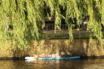 Ein Mann liegt auf einem Paddleboard auf einem Alsterkanal unter einem Baum: Am Sonntag sollte man sich besser nur im Schatten aufhalten.