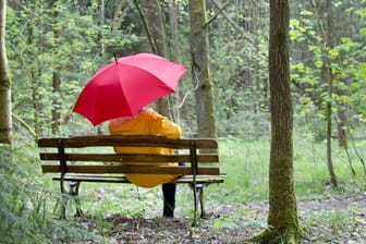 Frau sitzt mit Regenschirm auf einer Bank: Der Stoff sollte vollständig getrocknet sein, ehe Sie den Regenschirm wieder zusammenpacken.