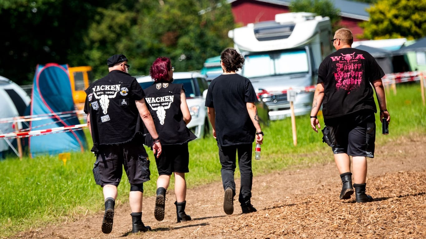 Besucher vom Heavy-Metal-Festival Wacken Open Air (W:O:A) gehen über einen Campingplatz.