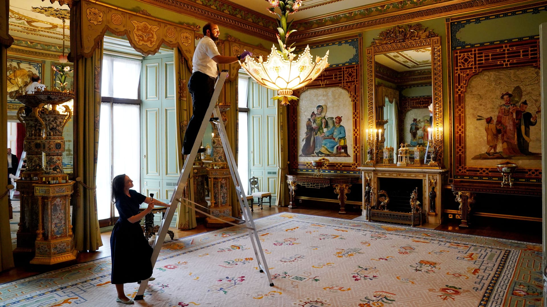 Letzte Vorbereitungen werden im Centre Room getroffen, wo sich Mitarbeiter des Royal Collection Trust um einen Kronleuchter im Ostflügel des Buckingham Palace, London, kümmern.