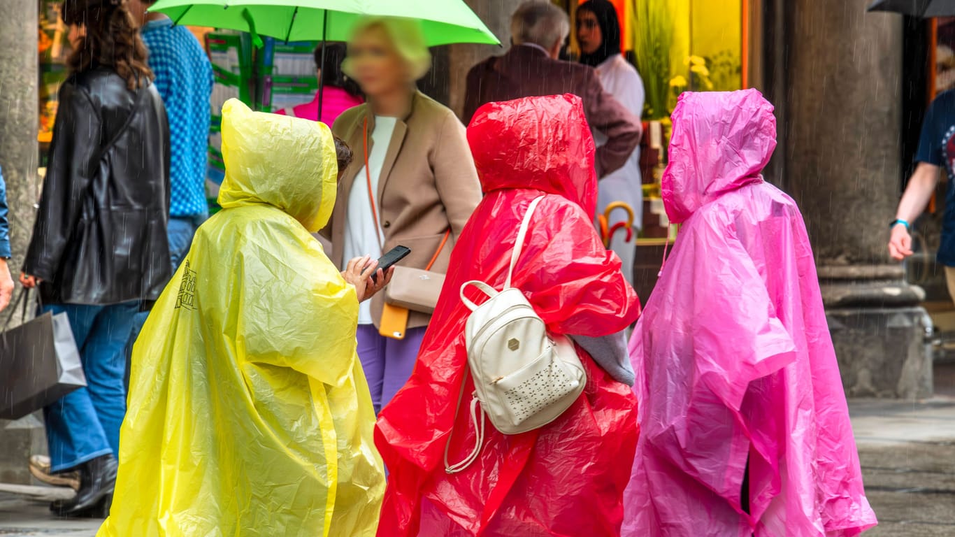 Frauen mit Regenponchos in der Münchner Fußgängerzone: Fieses Wetter im Juli 2024.