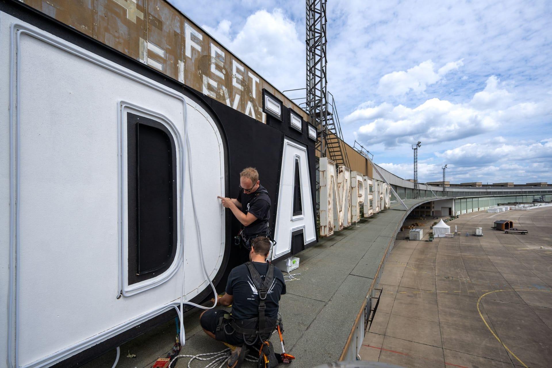 05.07.2024, Berlin: Zwei Mitarbeiter befestigen die Buchstaben des abgeänderten Schriftzuges "Berlin - DÄmpelhof" über dem ehemaligen Abfertigungsbereich des Flughafens Berlin-Tempelhof. Für einen Tag durfte die Band Die Ärzte im Vorfeld ihrer Konzerte am 23., 24. und 25. August 2024 den Schriftzug auf dem denkmalgeschützten Bau abändern