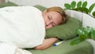 Frau liegt krank im Bett, neben ihr ein Fieberthermometer