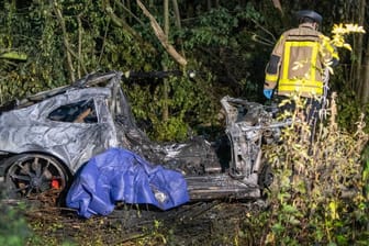 Ein Feuerwehrmann steht im Grünstreifen der A44 neben dem Wrack eines ausgebrannten Sportwagens: Zwei Insassen des Wagens sind bei dem Unfall ums Leben gekommen.