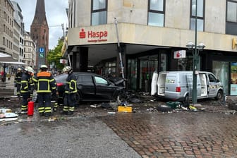 Helfer stehen an einem demolierten Auto vor der Hamburger Sparkasse (Haspa) am Jungfernstieg. Ein Auto ist in Hamburg in eine Sparkasse gefahren, es gab mehrere Verletzte.