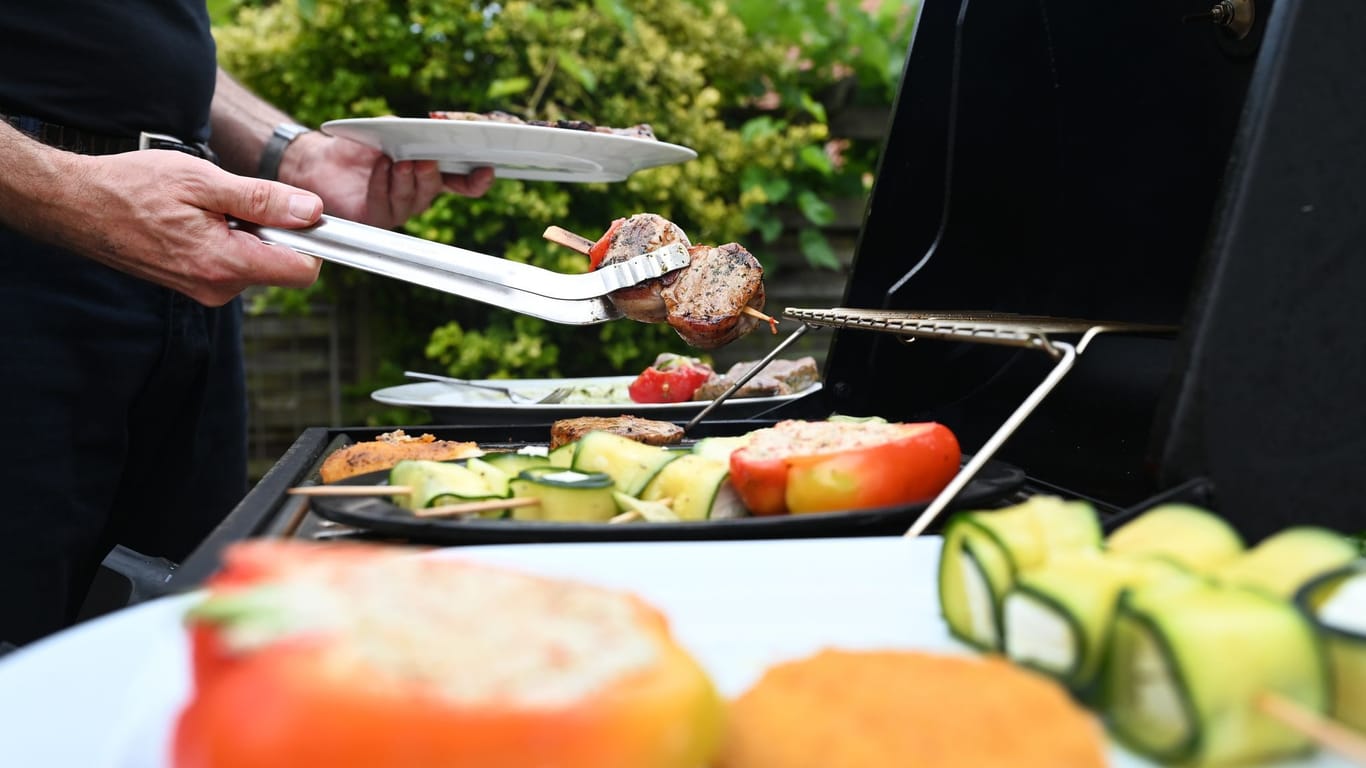 Eine Mann wendet mit einer Zange Grillfleisch auf einem Gasgrill