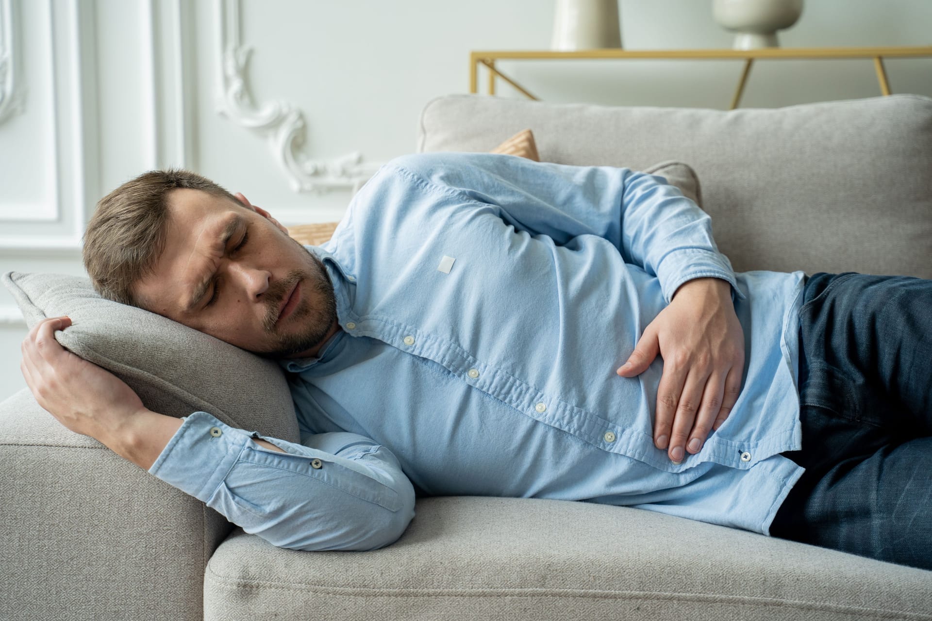 Mann liegt auf Sofa und hält sich den Magen-Darm-Bereich