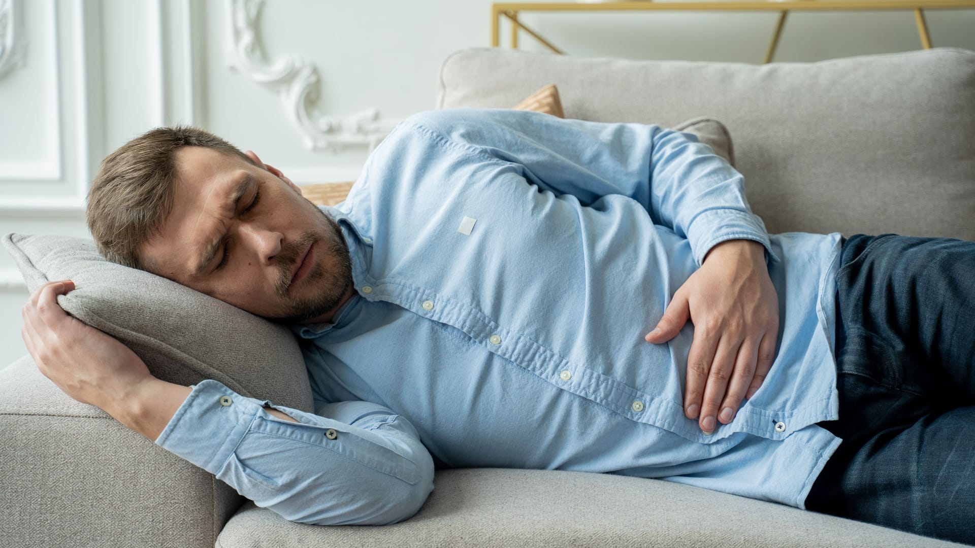 Mann liegt auf Sofa und hält sich den Magen-Darm-Bereich