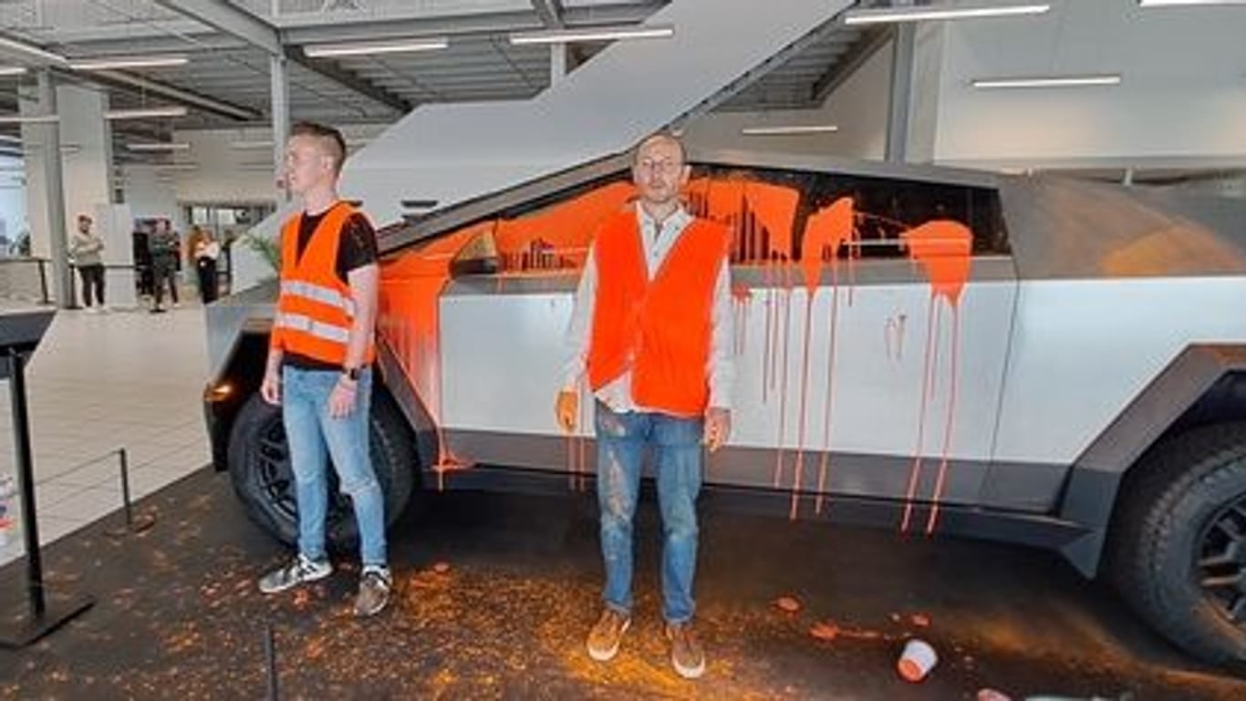 Zwei Aktivisten der "Letzten Generation" kurz nach dem Überkippen des Cyber Trucks mit oranger Farbe.