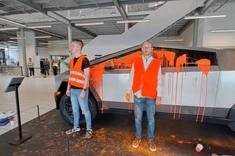 Zwei Aktivisten der "Letzten Generation" kurz nach dem Überkippen des Cyber Trucks mit oranger Farbe.