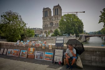 Ein Mann sitzt unweit der Notre-Dame mit einem Sonnenschirm (Archivbild): In den kommenden Tagen wird es in Paris heiß.