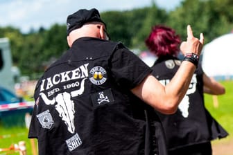 Ein Besucher vom Heavy-Metal-Festival Wacken Open Air geht über einen Campingplatz und zeigt mit gerecktem Zeigefinger und kleinem Finger den Wacken-Gruß.