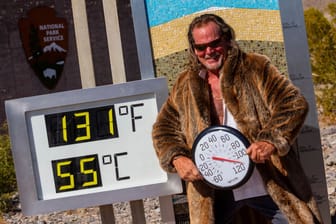Hitzewelle im Death Valley in den USA: Ein Mann posiert in einer Pelzjacke neben einem Thermometer, das eine Temperatur von 55 Grad Celsius anzeigt.