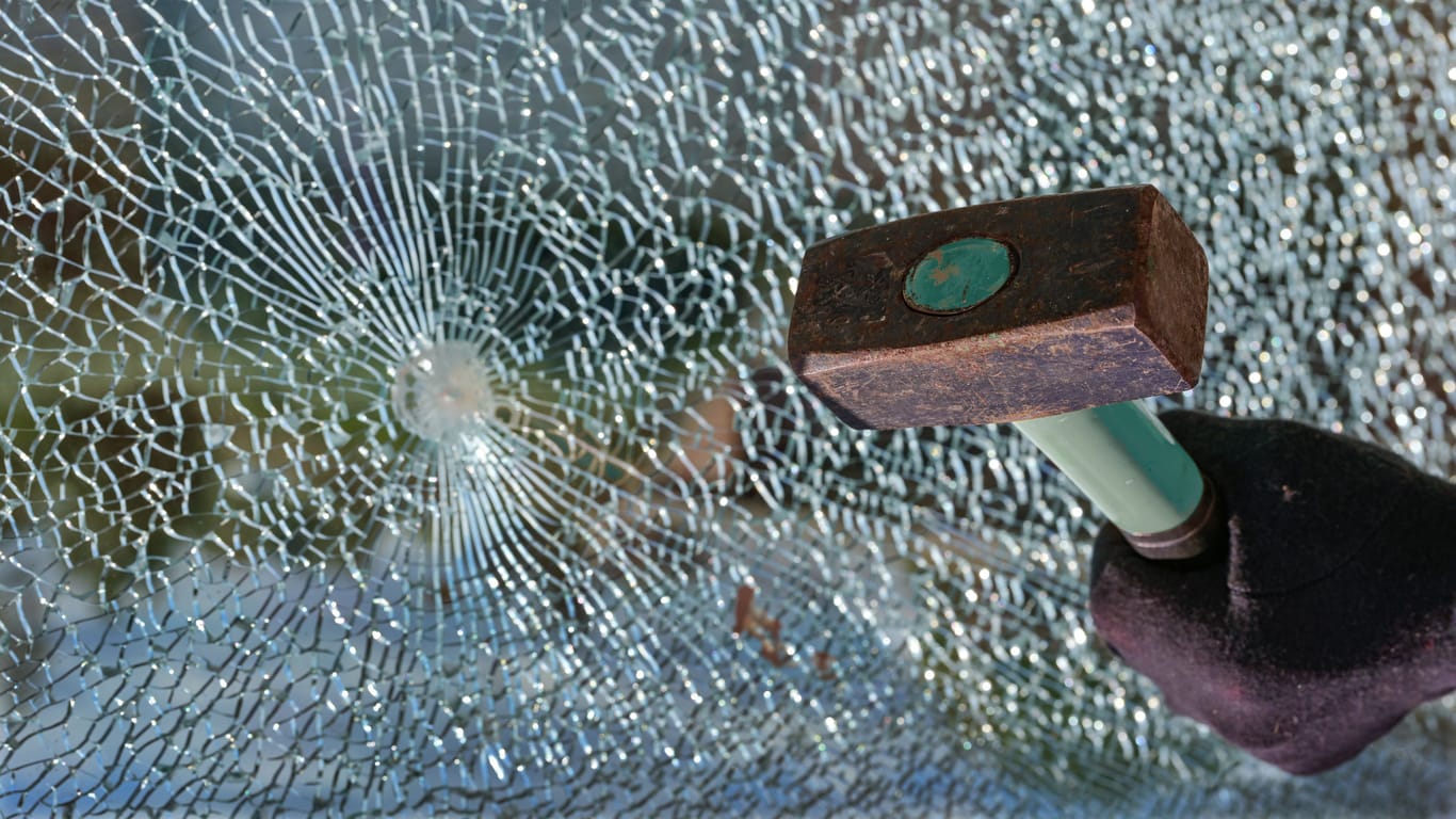 Hand with a hammer and a broken window made of safety glass, concept for burglary and vandalism