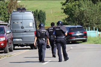 Polizisten in Schutzwesten gehen in Heiligkreuzsteinach über die Straße.