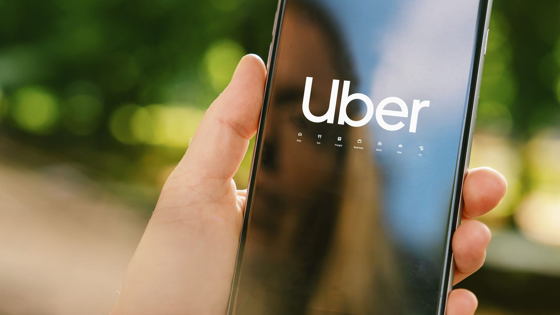 Uber driver holding smartphone in car. Uber is an American company offering different transportation services online