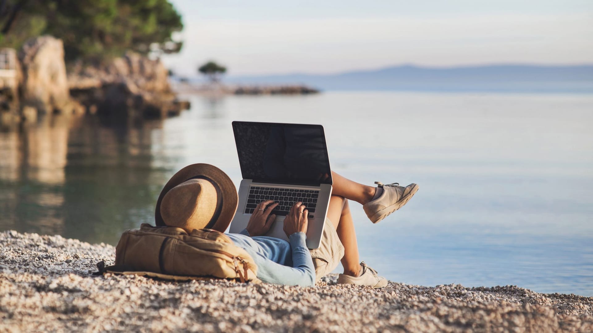 Person liegt am Strand und arbeitet auf einem Laptop