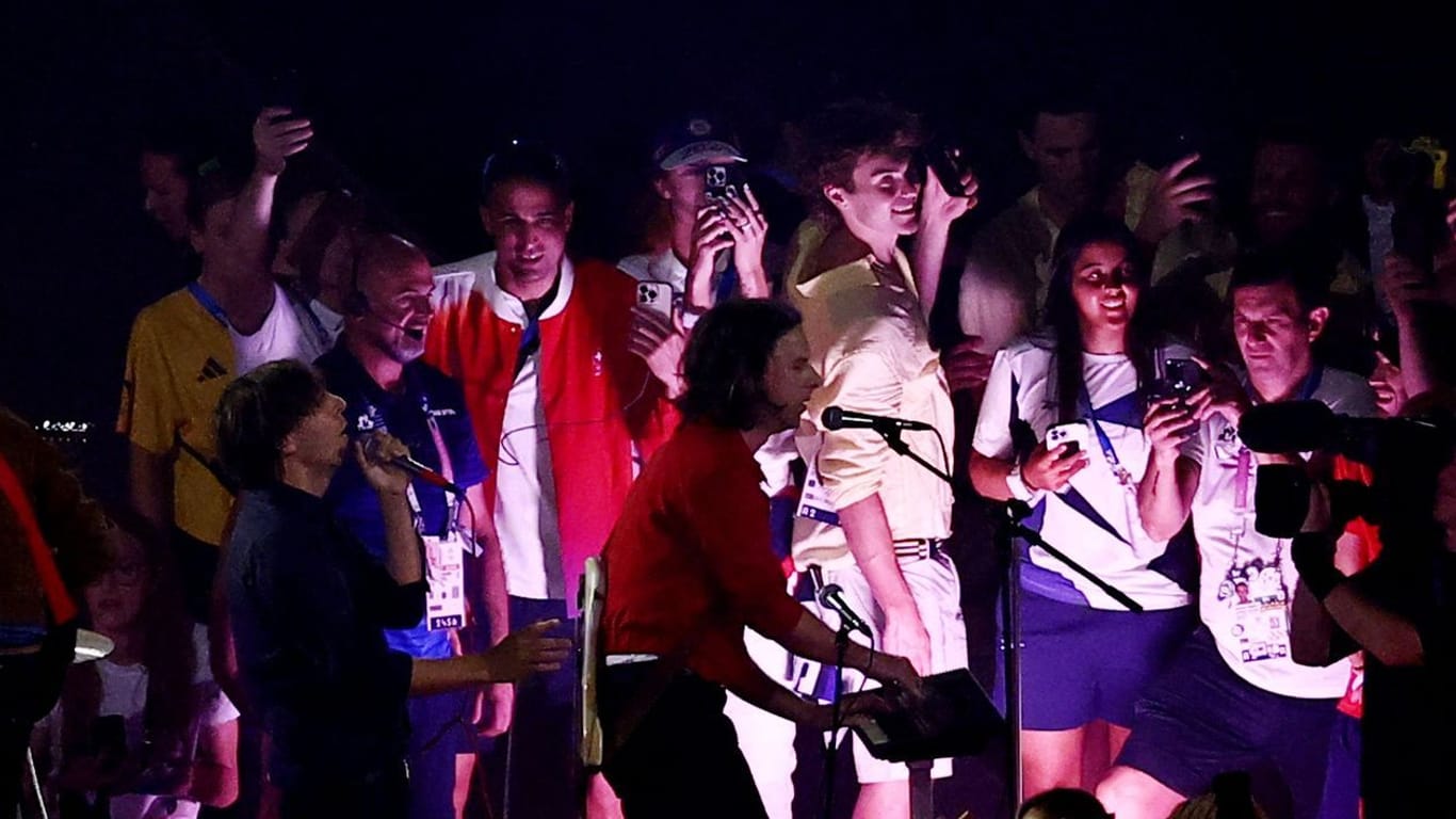 Athleten stehen neben der Band Phoenix auf der Bühne beim Abschluss der Olympischen Spiele.