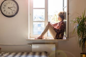 Frau sitzt auf dem Fensterbrett und genießt die frische Luft