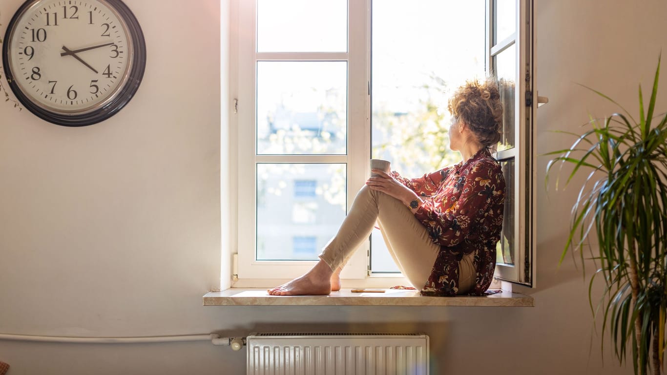 Frau sitzt auf dem Fensterbrett und genießt die frische Luft