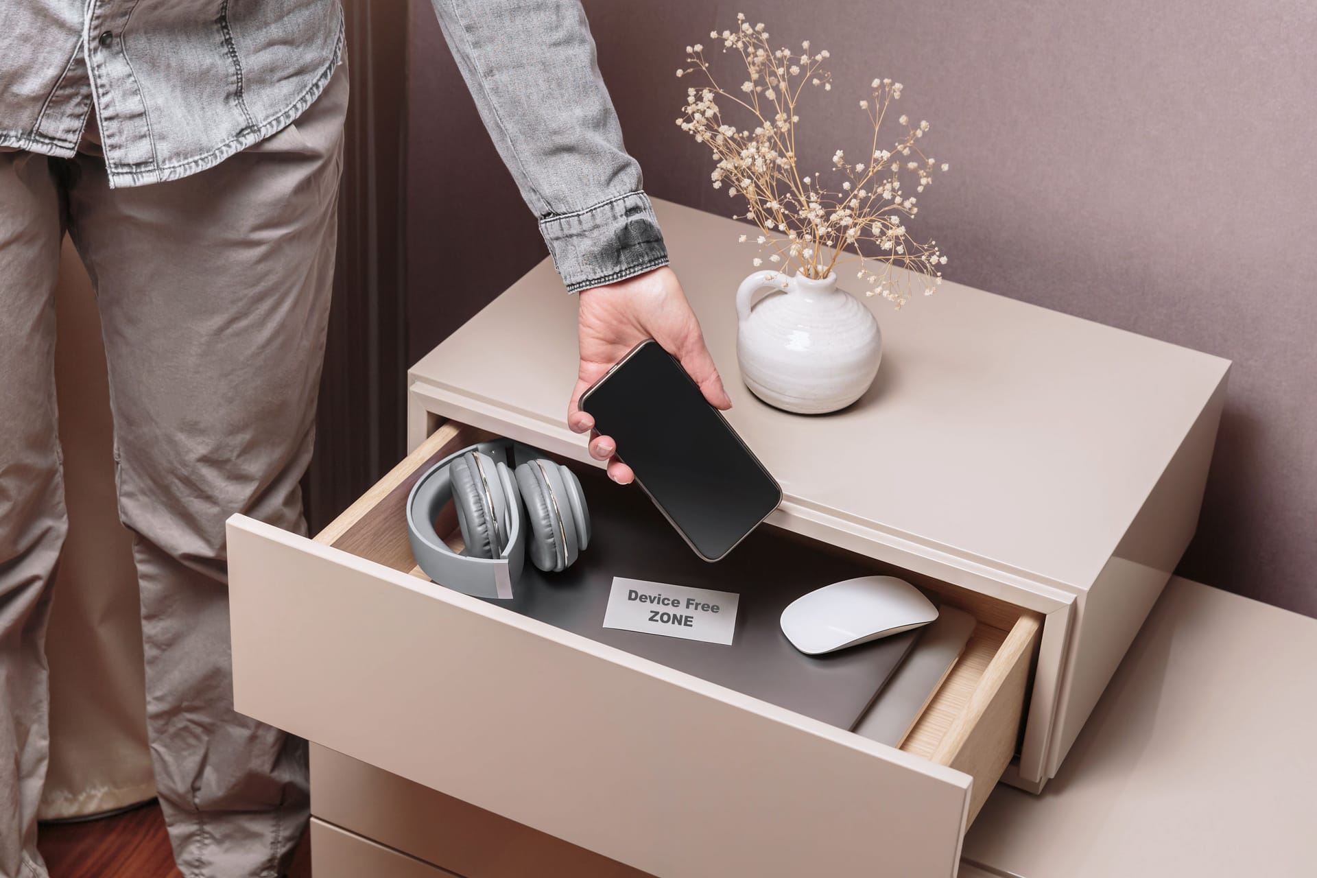 Woman putting her phone in drawer with different gadgets at home