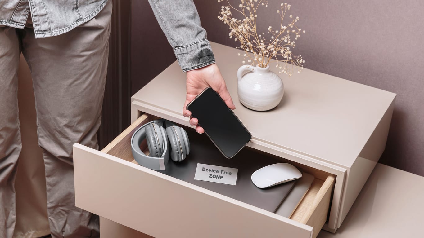 Woman putting her phone in drawer with different gadgets at home