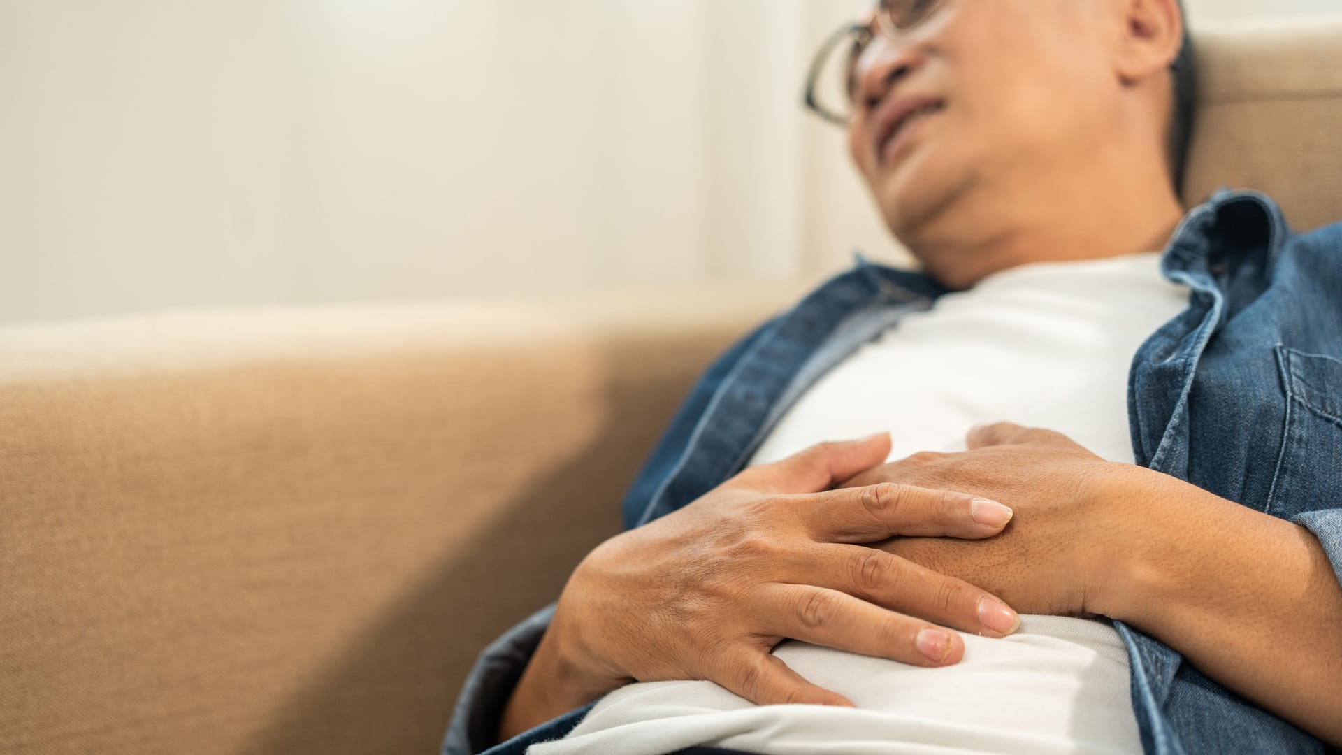 Mann liegt mit Bauchkrämpfen auf dem Sofa