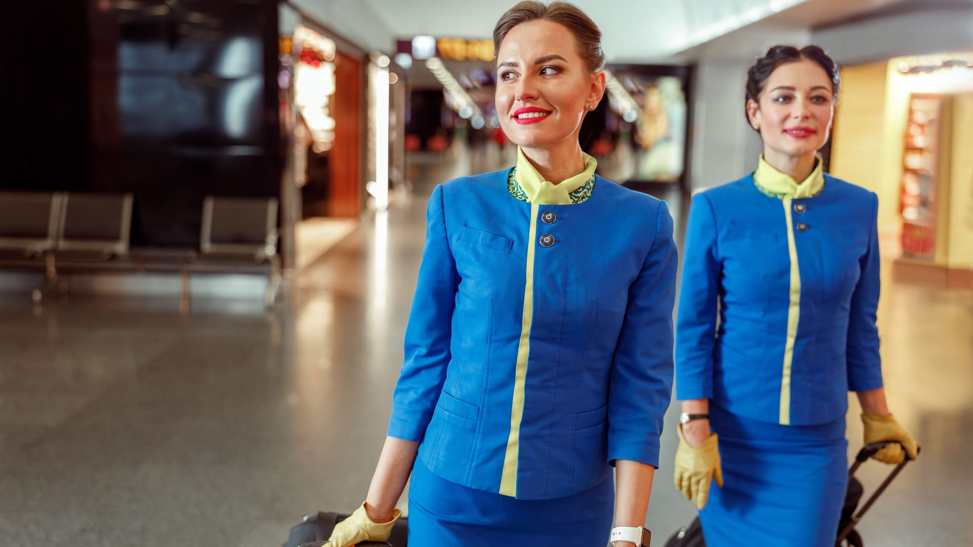 Cheerful women stewardesses carrying travel bags at airport