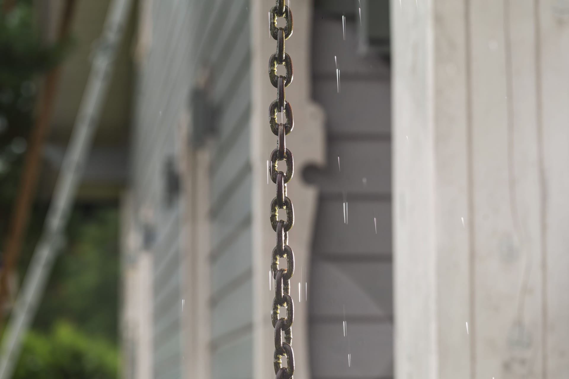 Rain chain and raindrops on the background of a Scandinavian style wooden house.