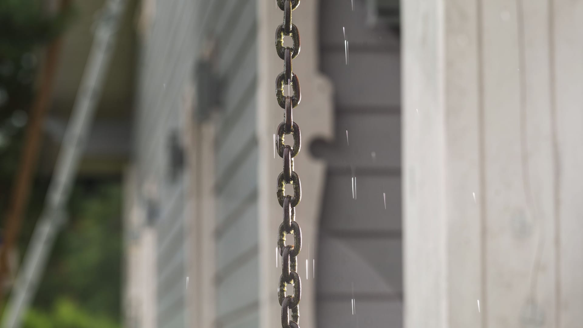 Rain chain and raindrops on the background of a Scandinavian style wooden house.