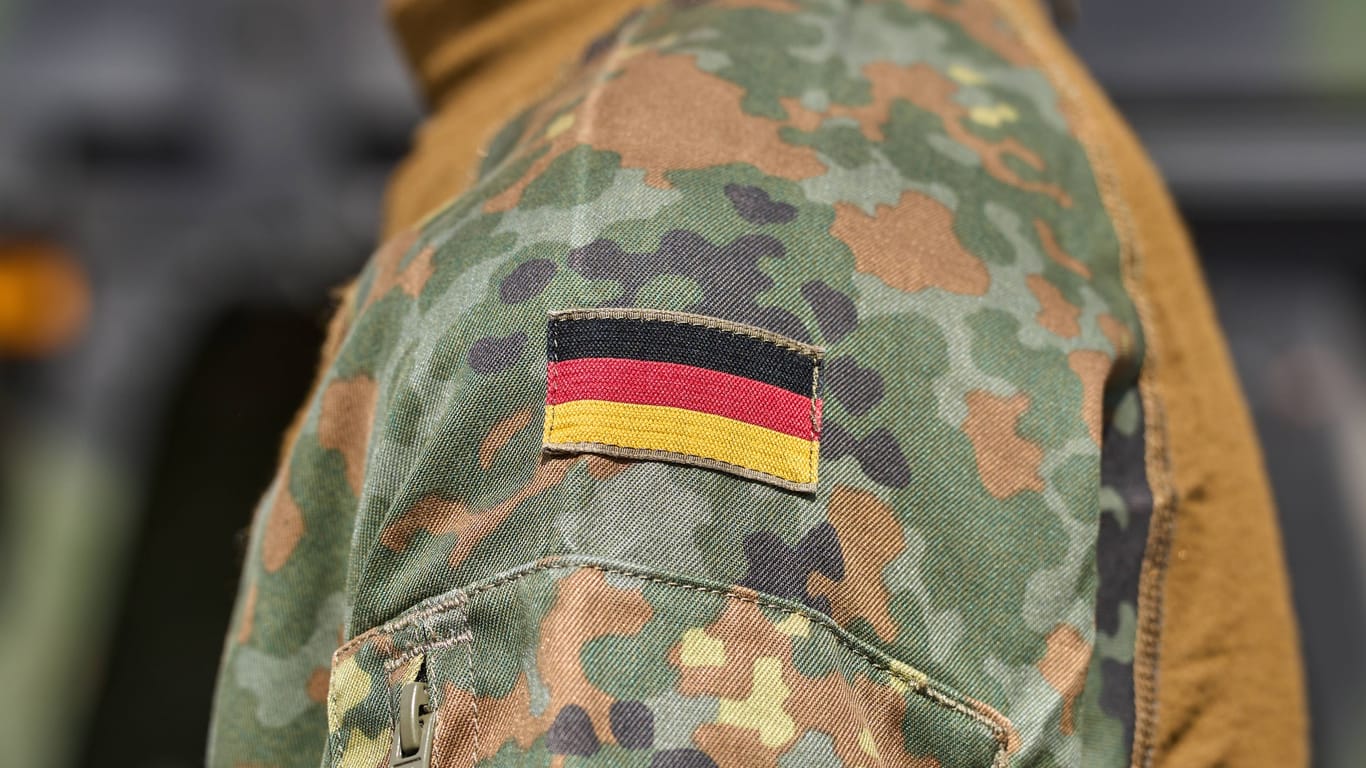 Soldat der deutschen Bundeswehr in Uniform vor einem Militärfahrzeug. Deutschland Flagge auf der Schulter der Bundeswehruniform