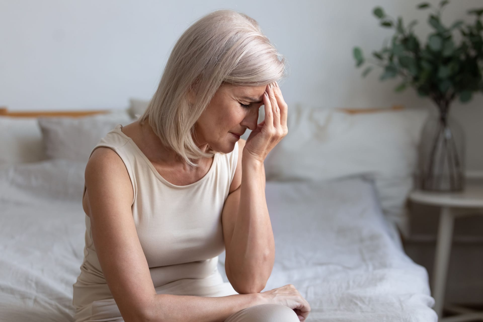 Frau sitzt auf dem Bett und fasst sich mit der Hand an die Stirn.