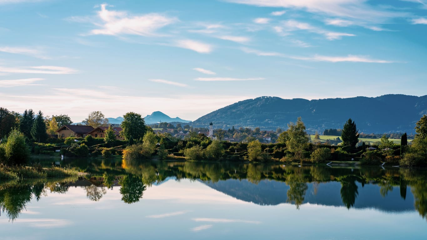 The village and church of Koenigsdorf in Bavaria with the Bibi Lake in the foreground and the mountains in the background