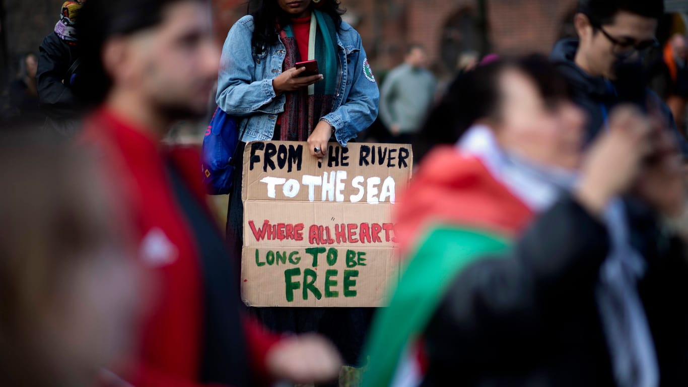 Ein Demonstrant hält ein Plakat mit dem Spruch "From The River To The Sea Where All Hearts Long To Be Free" in der Hand: