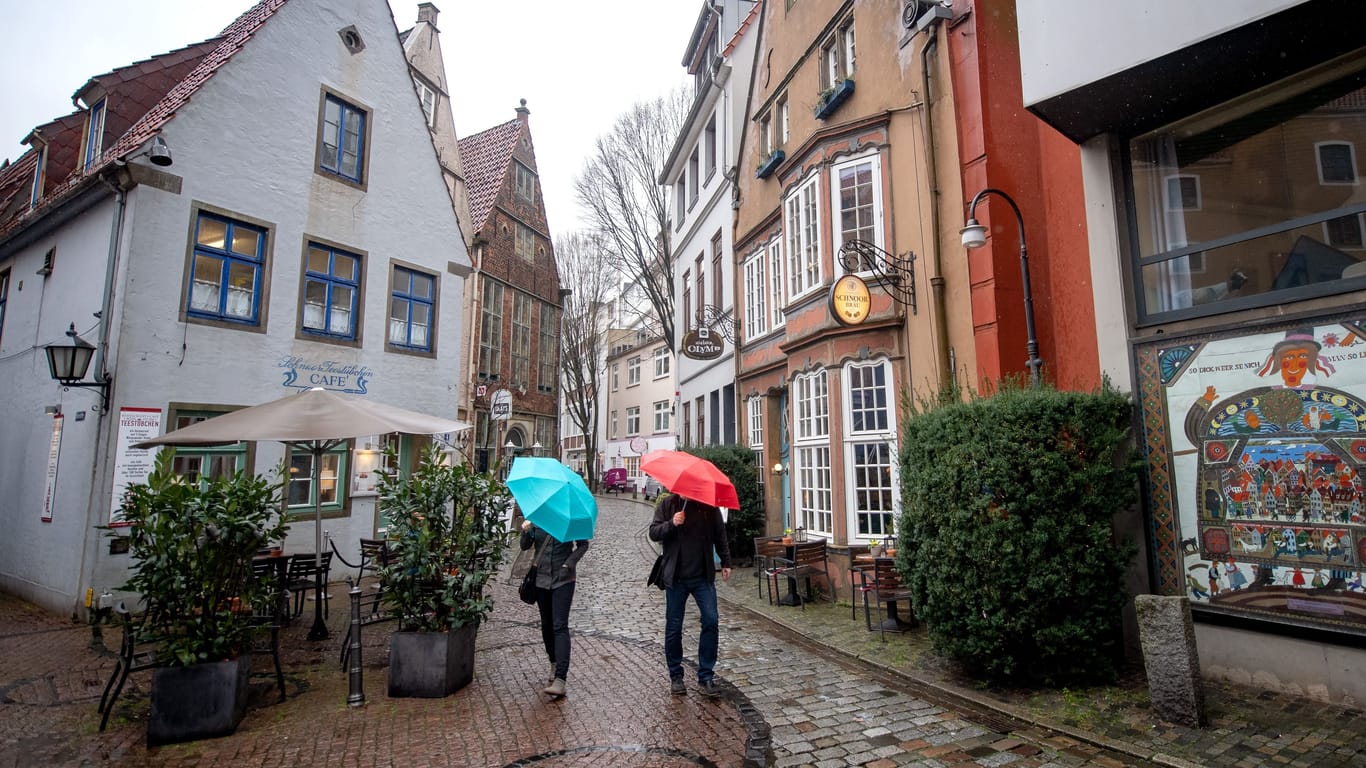 Menschen mit Regenschirmen laufen bei Regen durchs Schnoorviertel in Bremen.