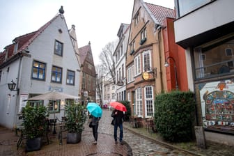 Menschen mit Regenschirmen laufen bei Regen durchs Schnoorviertel in Bremen.