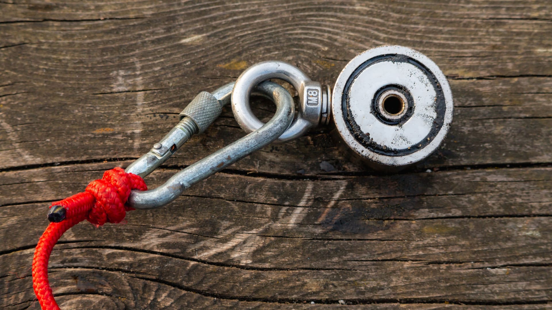 Strong magnet on a red rope carabiner, on a wooden surface. Equipment for magnet fishing