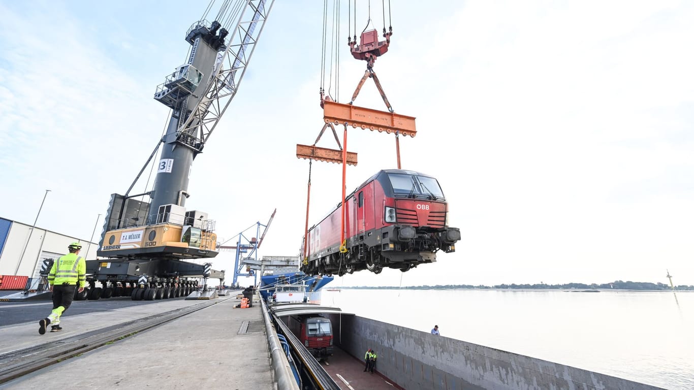 Eine E-Lok von Rail Cargo Carrier Germany (RCC) wird mit zwei Kränen auf das Binnenschiff "Rolf-Hein" gehoben und auf dem Seeweg nach Bremen transportiert.