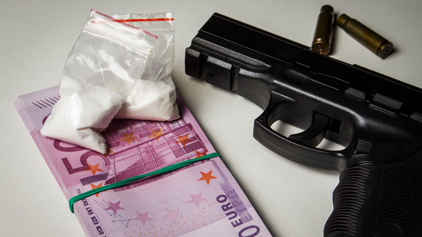 Black gun with a pack of euros and packets of drugs on a white table