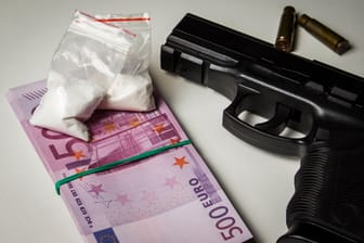 Black gun with a pack of euros and packets of drugs on a white table