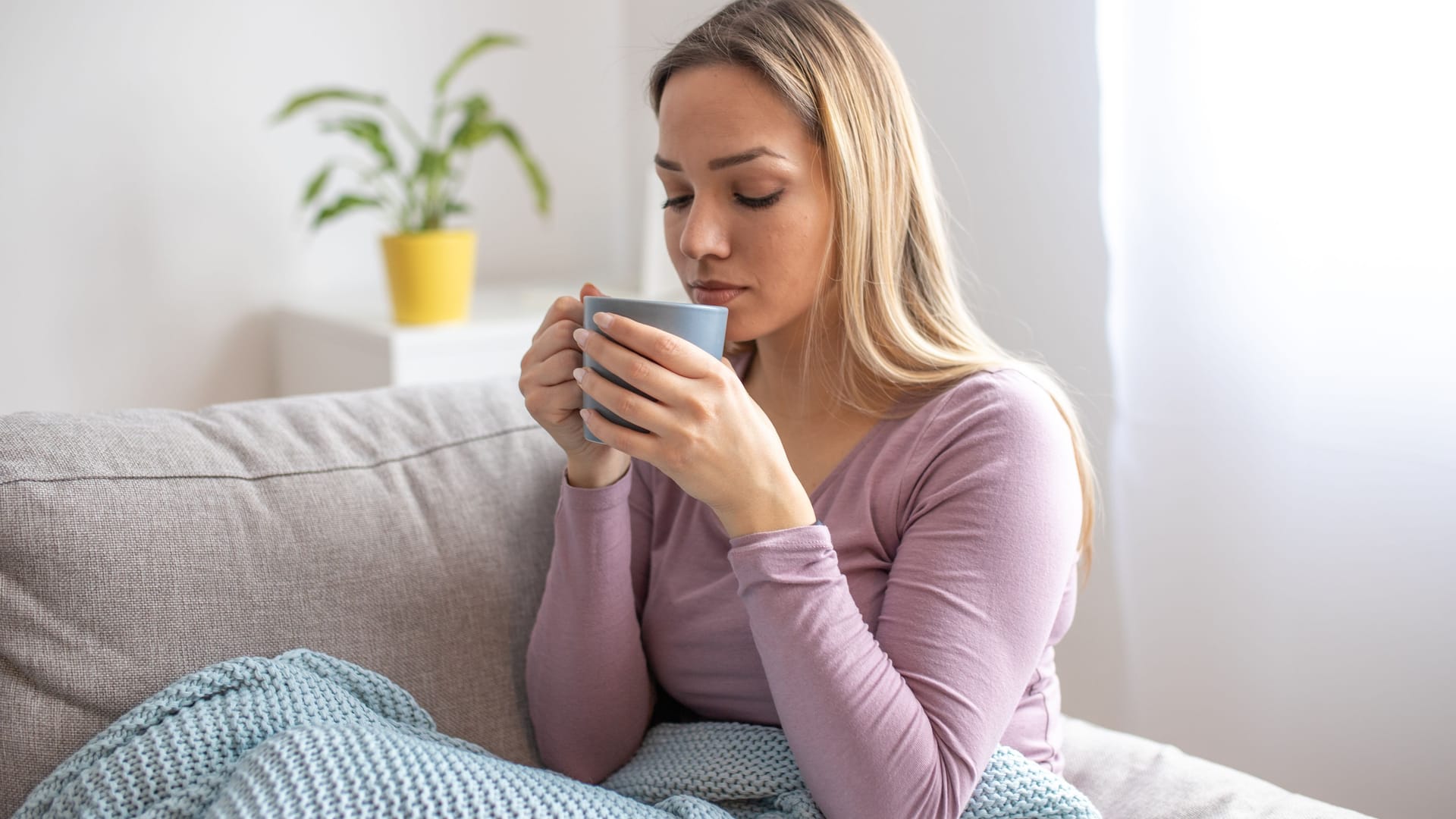 Junge Frau sitzt auf dem Sofa und trinkt Tee.